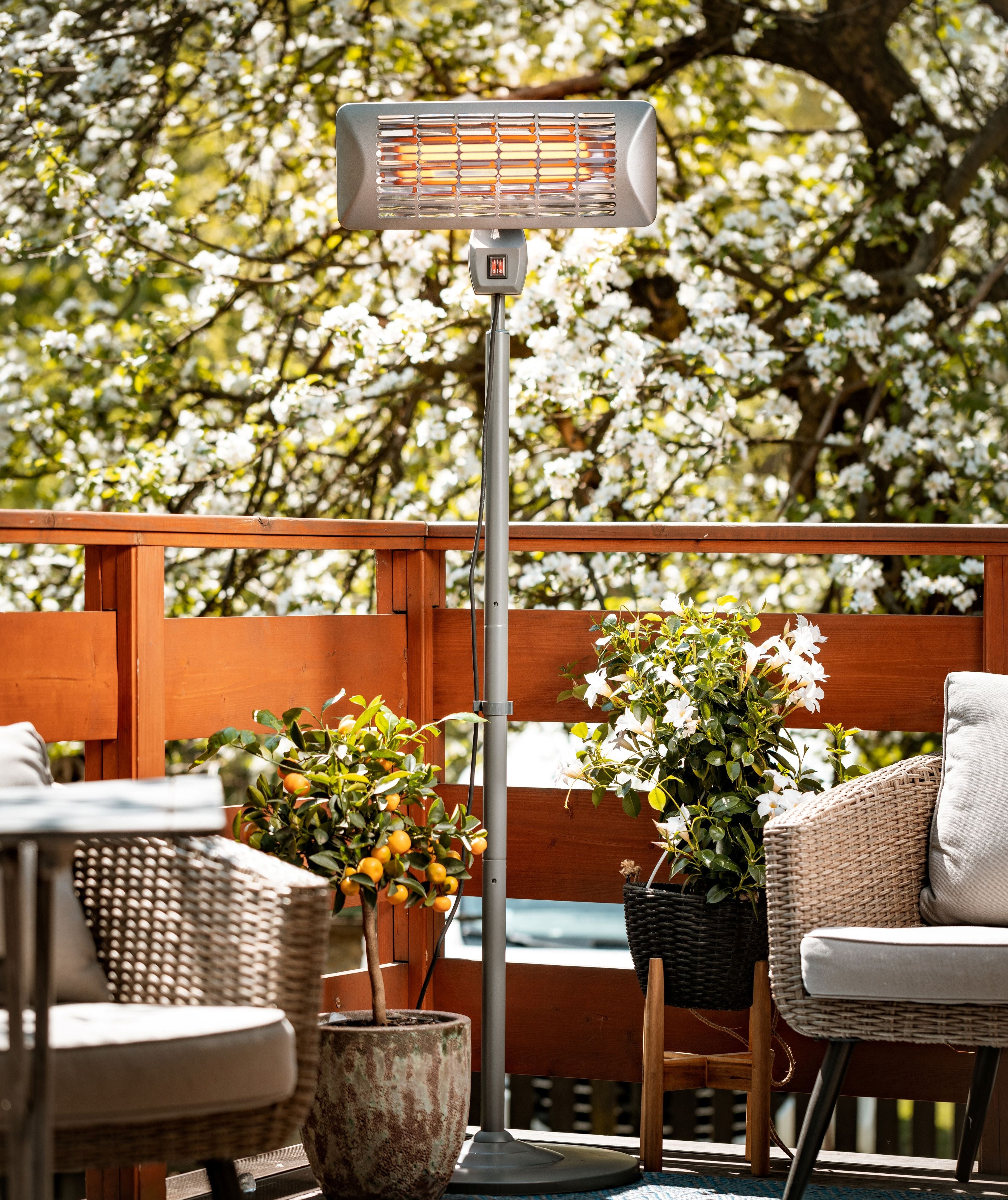 Outdoor patio heater on a wooden deck with chairs and plants in the background